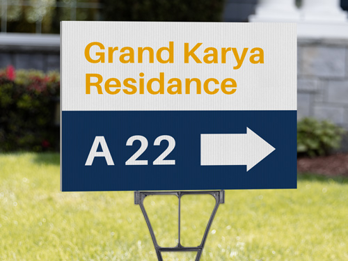House number yard sign on a green lawn featuring bold white and yellow text displaying the address, set against a blue background with simple decorative elements