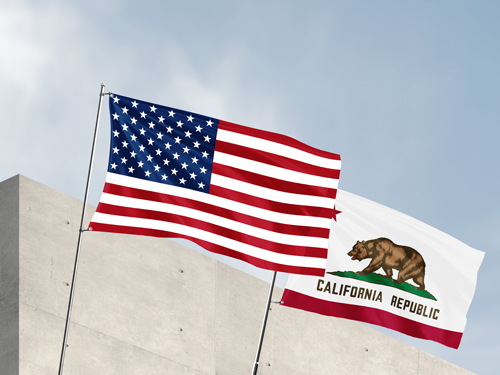 American and California Republic pole flags waving side by side above a concrete building.
