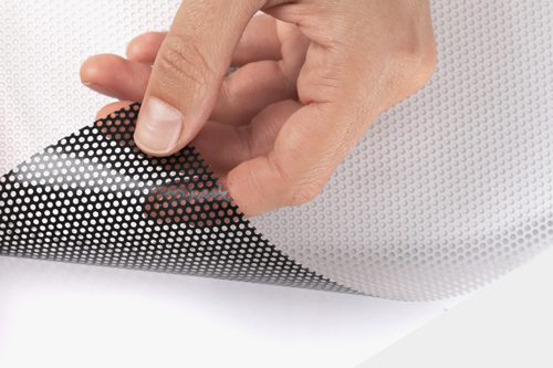Close-up of a hand peeling a perforated window decal from a white surface.