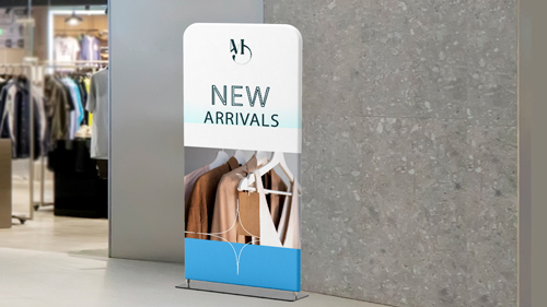 Retail standing banner with New Arrivals text showing clothing rack in background