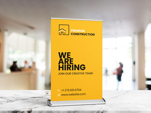 Yellow tabletop retractable banner showing "We Are Hiring" and contact information.